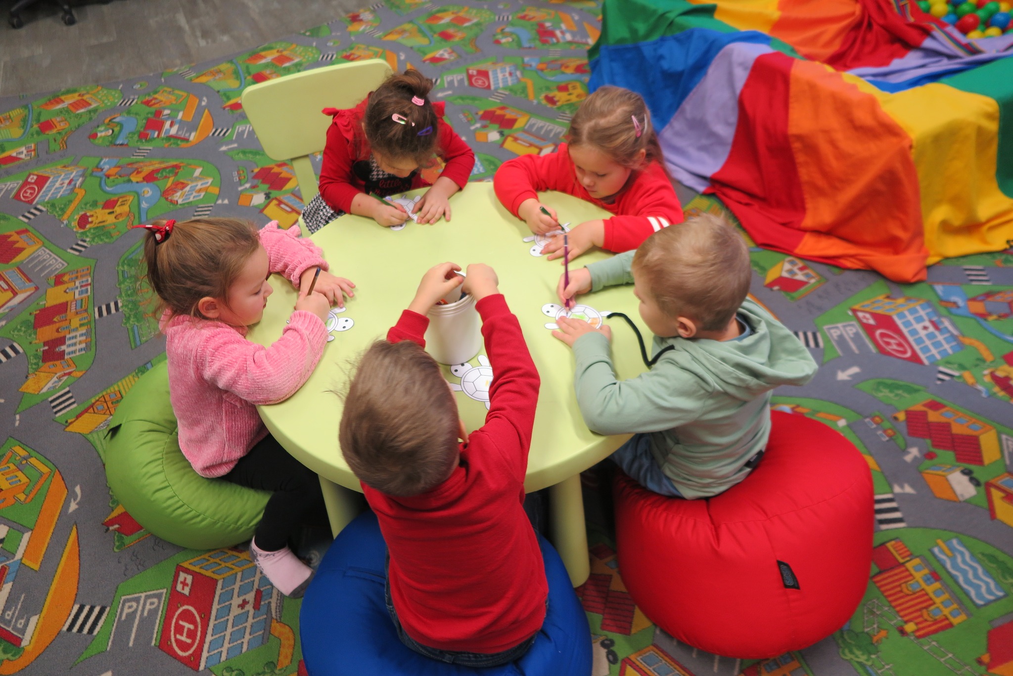 dzieci kolorują wycinankę siedząc przy okrągłym stoliku 