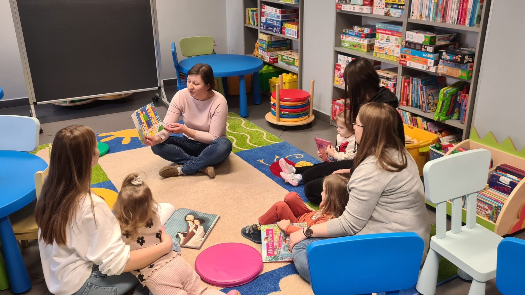 dzieci z rodzicami słuchają czytanej przez bibliotekarkę książki