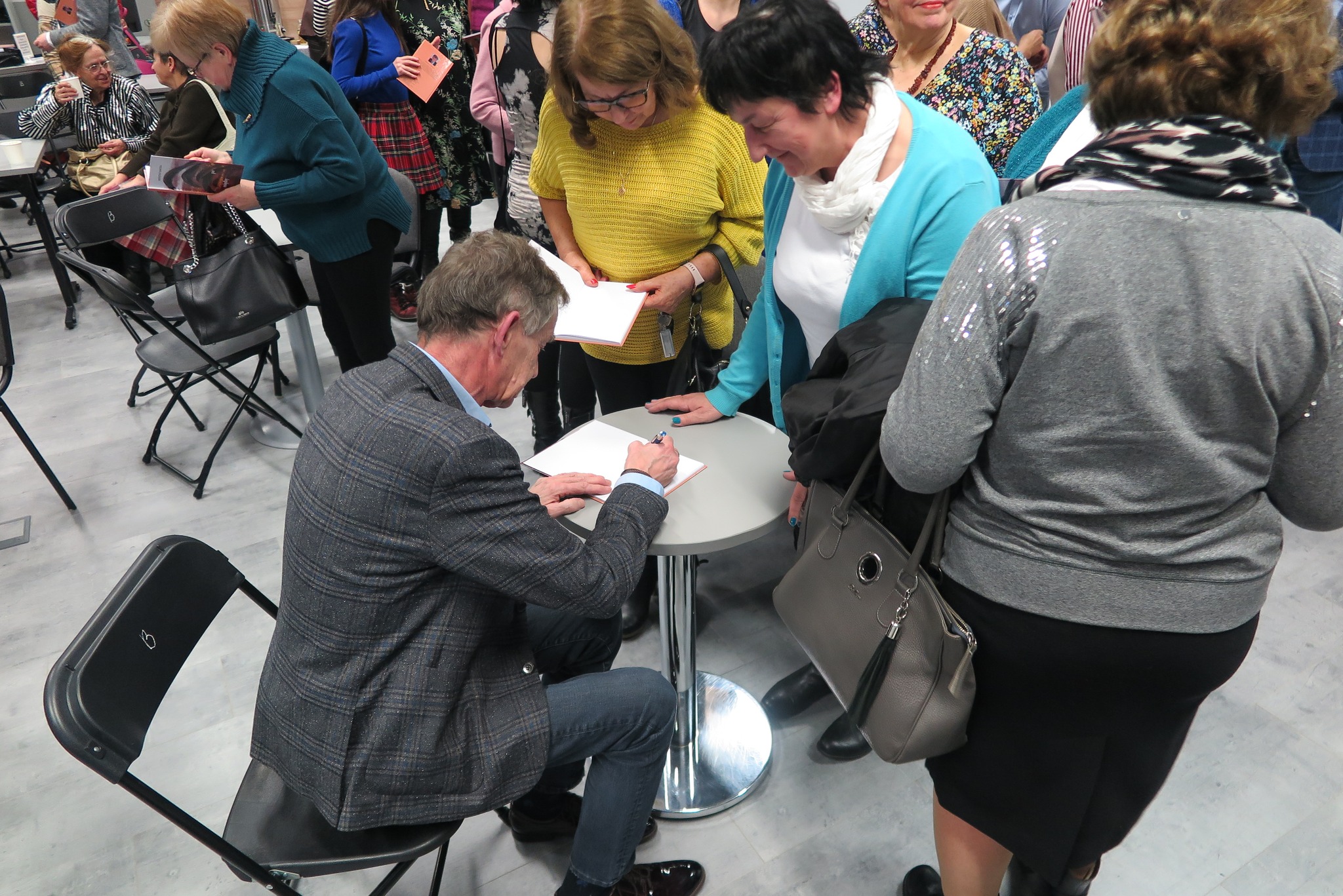 autor podpisuje książki publiczności siedząc przy okrągłym stoliku