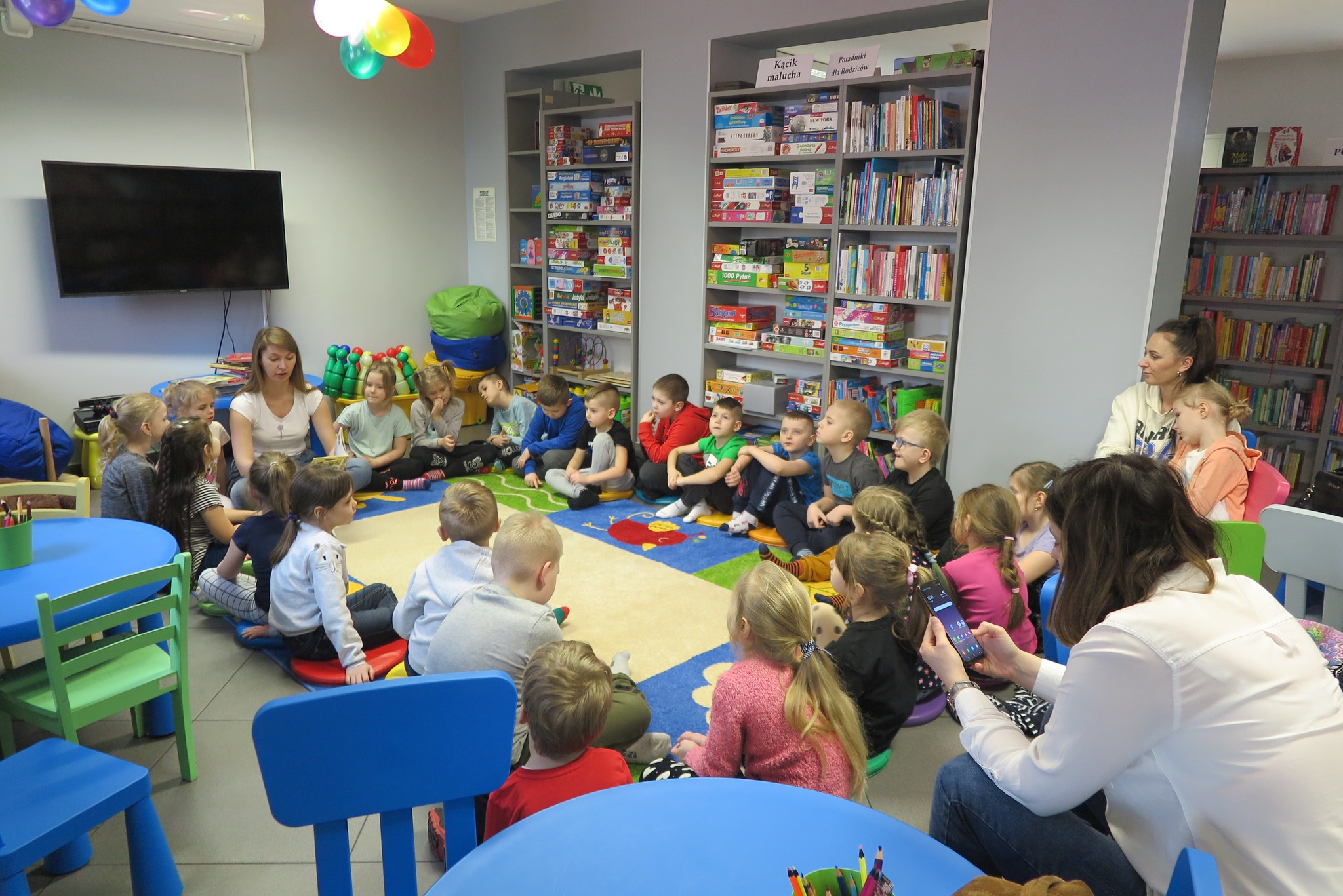 dzieci z przedszkola nr 5 siedzą na dywanie w oddziale dla dzieci i słuchaj czytanej przez bibliotekarkę książki