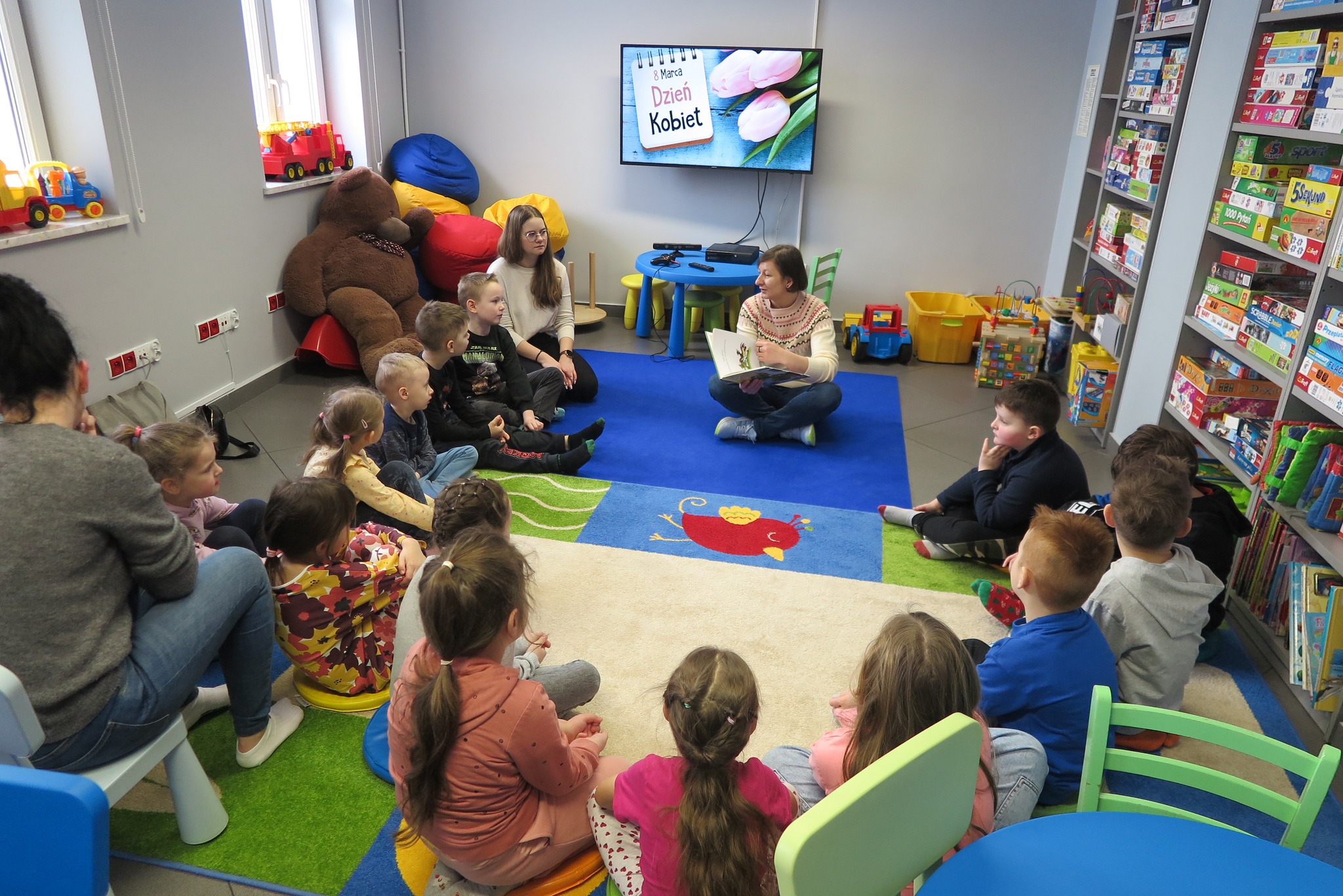 Dzieci z przedszkola słuchają czytanej przez bibliotekarkę książki z okazji Dnia kobiet "Franklin i nowa opiekunka"