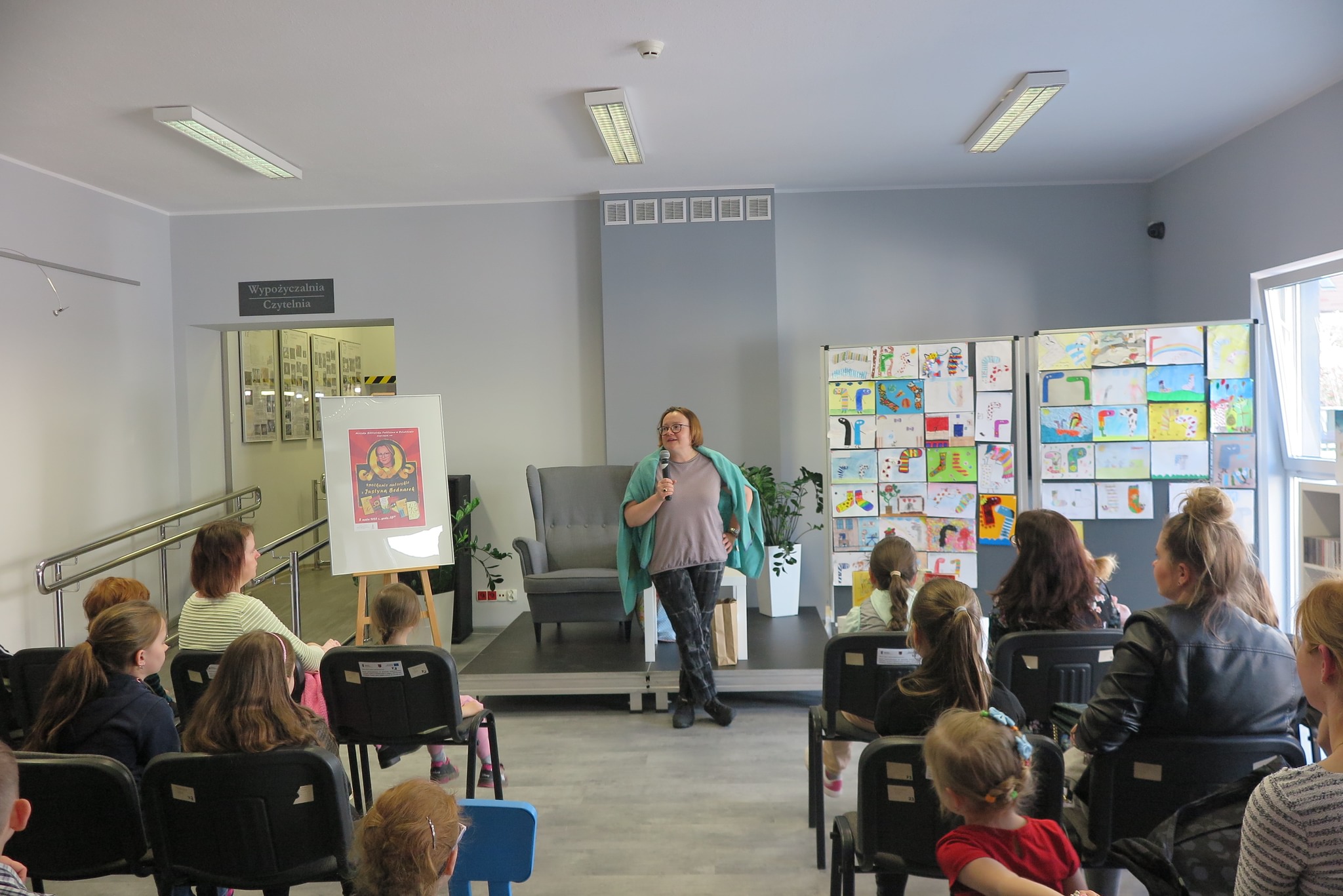 Justyna Bednarek podczas spotkania autorskiego stoi przed dziećmi uczestniczącymi w spotkaniu autorskim
