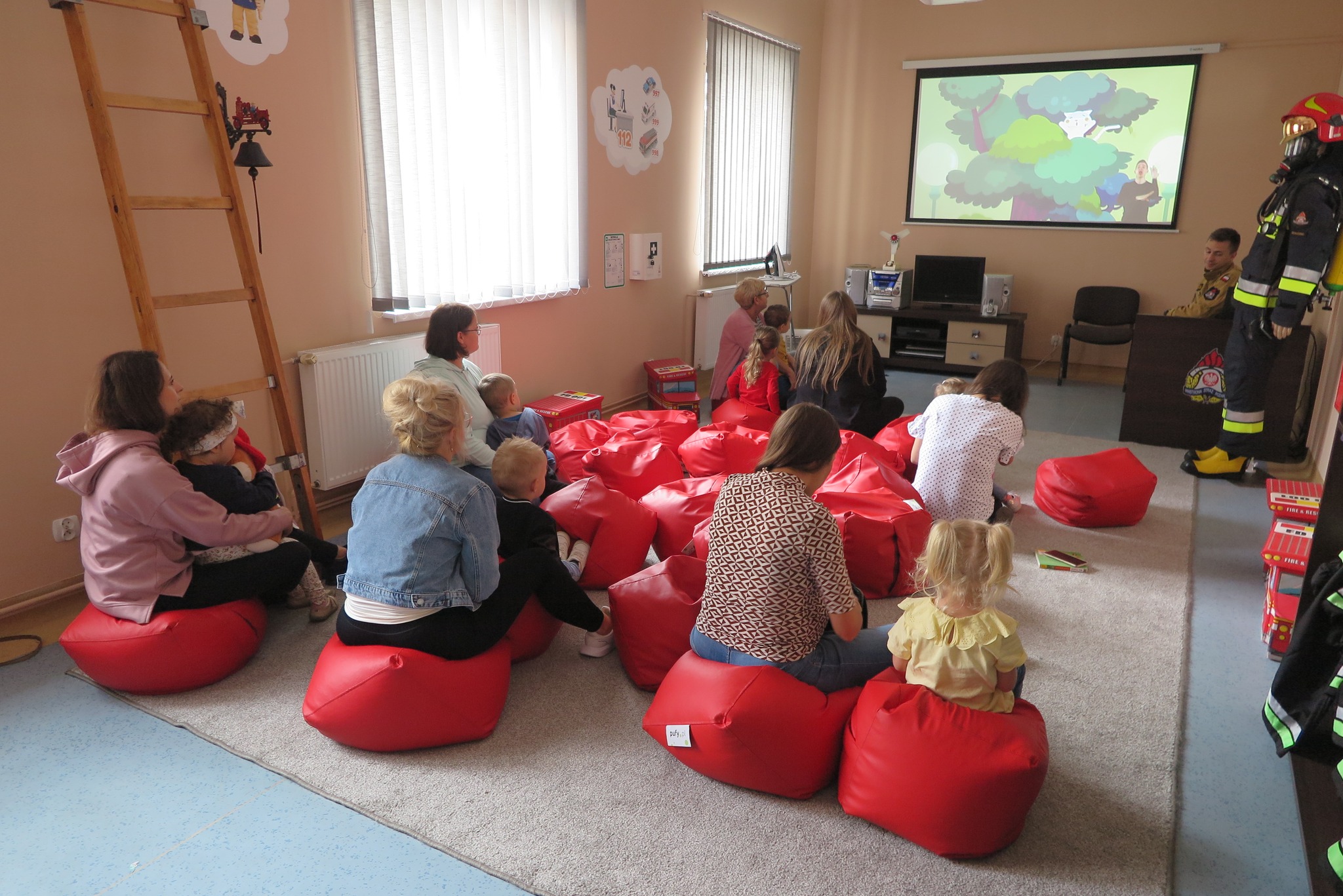dzieci z klubu malucha z rodzicami z wizytą w Powiatowej Straży Pożarnej w Działdowie oglądają prezentację na ekranie