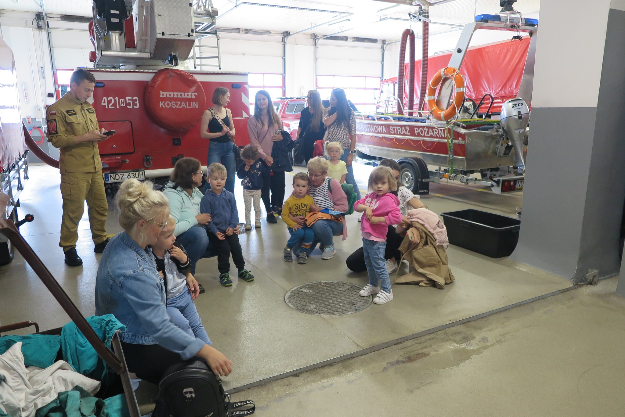 dzieci z klubu malucha z rodzicami z wizytą w Powiatowej Straży Pożarnej w Działdowie oglądają pojazdy gaśnicze w garażu straży