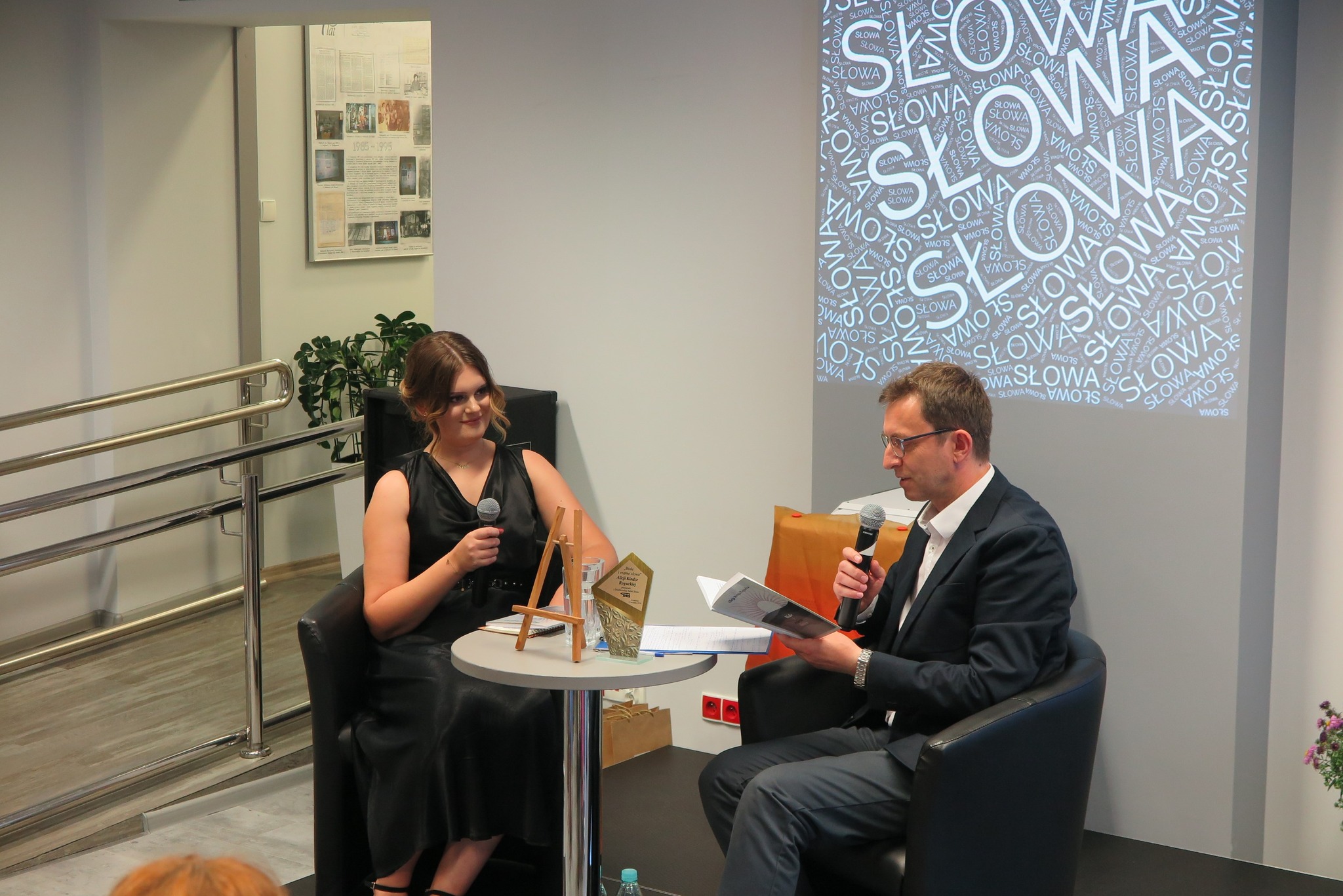Alicja Ragucka i Piotr Kozikowski siedzą w fotelach na scenie, oboje trzymają mikrofony w ręku